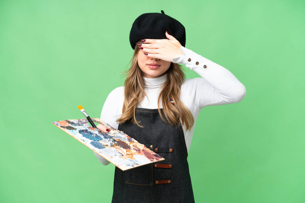 Young artist girl holding a palette over isolated chroma key background covering eyes by hands. Do not want to see something - Photo, Image