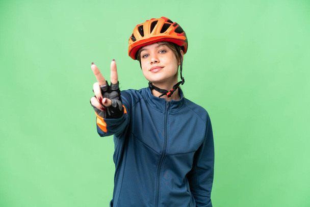 Young cyclist girl over isolated chroma key background smiling and showing victory sign - Zdjęcie, obraz