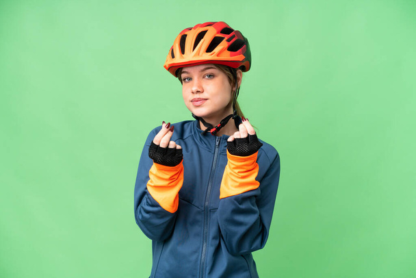 Young cyclist girl over isolated chroma key background making money gesture - Foto, Imagen