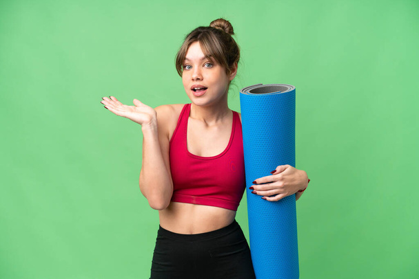 Young sport girl going to yoga classes while holding a mat over isolated chroma key background with shocked facial expression - Foto, Imagem