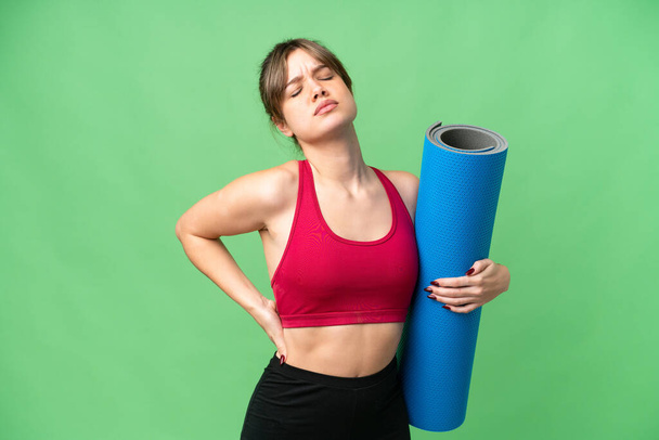 Young sport girl going to yoga classes while holding a mat over isolated chroma key background suffering from backache for having made an effort - Foto, Imagen