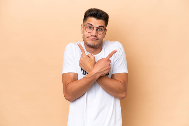 Young volunteer caucasian man isolated on beige background pointing to the laterals having doubts - Foto, Bild