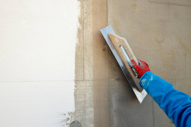 Bauherr verputzt die Wand mit einem Spachtel, Glasfasernetz, nachdem er das Haus gedämmt hat - Foto, Bild