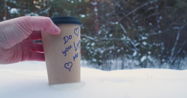 Man en vrouw handen zet papieren beker met koffie in de sneeuw met inscripties hou je van mij en ja. Liefde en relaties concept. Slow motion 4k beeldmateriaal. - Video