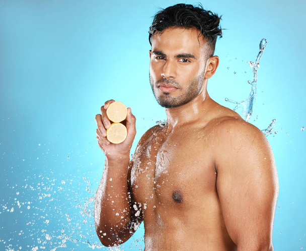 Lemon, skincare and portrait of man in water splash in studio for wellness, cleaning and fresh on blue background. Fruit, product and beauty by male model relax with luxury, facial and skin treatment. - Fotografie, Obrázek