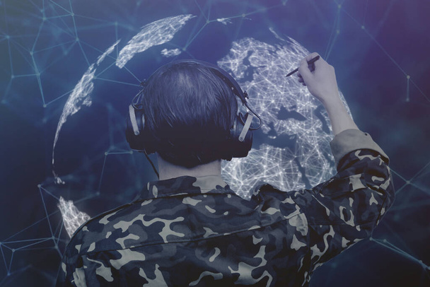 A military cartographer with headphones marks a glowing dot on the world map. Concept: development of a plan of capture and attack, the war in Ukraine, a military operation. - Foto, imagen