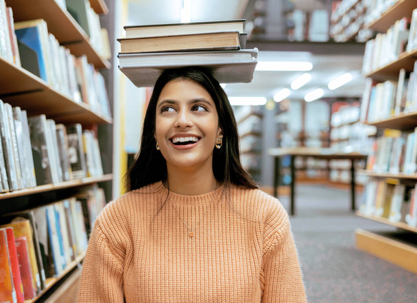 Books, balance or happy student in a library reading for knowledge or development for future growth. Scholarship, portrait or funny school girl smile while studying or learning college information. - 写真・画像