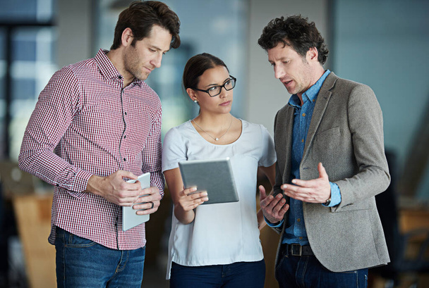 Poner en práctica su plan. un grupo de compañeros de trabajo de pie en una oficina hablando por una tableta digital - Foto, imagen