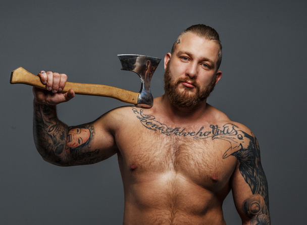 Жорстокий великий чоловік з татуюваннями і бородою тримає сокиру
 - Фото, зображення