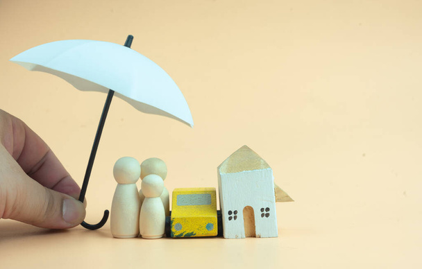 Close up image of wooden toy house, car and doll cover with white umbrella. Life insurance concept, home insurance. - Photo, Image