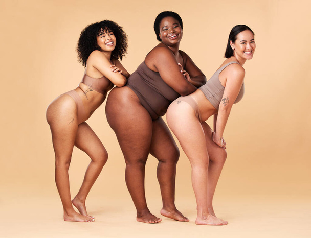 Diversity women, body size and portrait of group together for inclusion, beauty and power. Underwear model friends happy on beige background with cellulite legs, skin pride and self love motivation. - 写真・画像