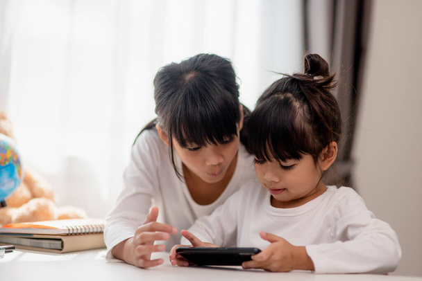 Concept kids and gadgets. Two little girls siblings sisters look at the phone and smile. They hold a smartphone watch videos, learn, play games, speak online. Internet for children. Parental control - Photo, Image