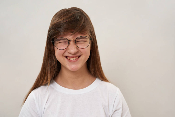 Cropped view of smiling caucasian teenage girl with closed eyes. Female child of zoomer generation wearing glasses. Modern youngster lifestyle. Isolated on white background. Studio shoot. Copy space - Φωτογραφία, εικόνα