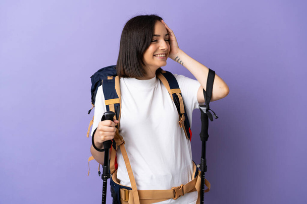 Young caucasian woman with backpack and trekking poles isolated on blue background smiling a lot - Φωτογραφία, εικόνα