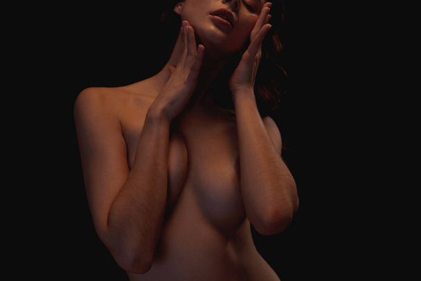 Partial image of sexy nude caucasian girl with closed eyes touching herself. Female beauty. Passion and desire. Pretty young slim brunette woman. Isolated on dark background. Studio shoot. Copy space - Foto, imagen