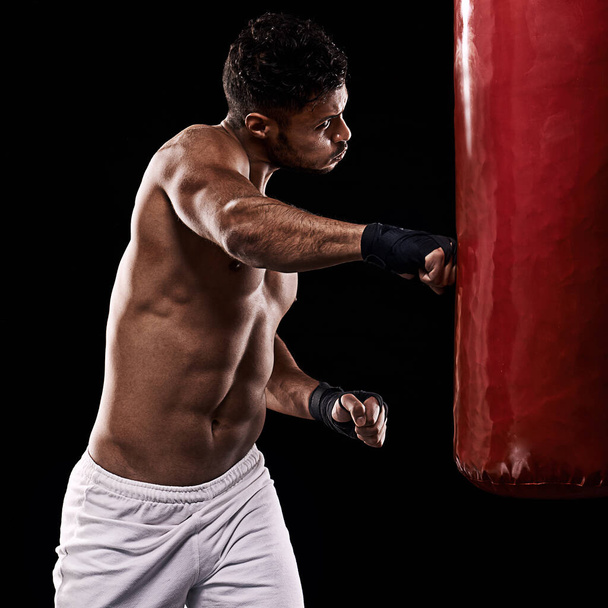 The harder you train the shorter the fight. Studio shot of kick boxer working out with a punching bag against a black background - Photo, image