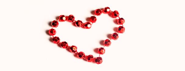 The heart is lined with red beads on a wooden table. A heart is lined with beads on the table. Valentine's Day - valentine on the table with your own hands. - Fotografie, Obrázek