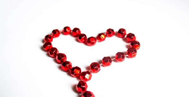 The heart is lined with red beads on a wooden table. Valentine's Day - valentine on the table with your own hands. A heart is lined with beads on the table. - Fotó, kép