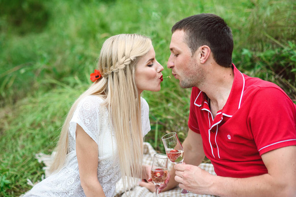 ζευγάρι ερωτευμένο μια ξανθιά κοπέλα και ένας τύπος με κόκκινο μπλουζάκι σε πικ-νικ σε ένα πάρκο με πράσινο γρασίδι - Φωτογραφία, εικόνα