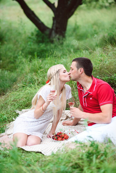 verliebtes Paar, ein blondes Mädchen und ein Mann im roten T-Shirt bei einem Picknick in einem Park mit grünem Gras - Foto, Bild