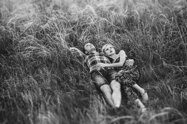 paar in liefde blond meisje en man in het gras bij zonsondergang - Foto, afbeelding