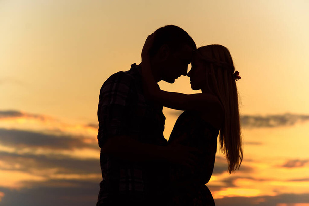 paar in liefde blond meisje in silhouet tegen een oranje zonsondergang - Foto, afbeelding