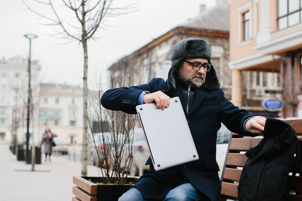 Vezető szabadúszó vagy menedzser dolgozik laptop, miközben ül padon a városban, míg az üzleti út. A munka koncepciója útközben. - Fotó, kép