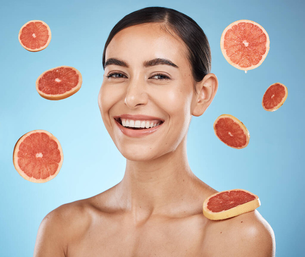 Woman, studio portrait and grapefruit with beauty skincare, smile or happy for wellness by blue background. Young gen z model, healthy face skin or citrus fruit for vitamin c with self care happiness. - Zdjęcie, obraz