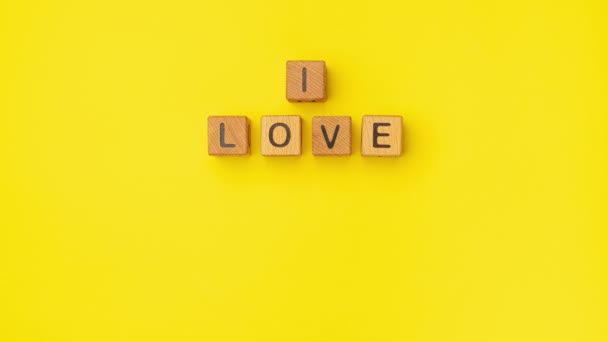 Drewniane kostki stop-motion ze zwrotem I Love You Może na pustym, kolorowym żółtym tle. Słowa miłości są zrobione z liter z drewna na Walentynki i dla twojej dziewczyny, chłopaka - Materiał filmowy, wideo