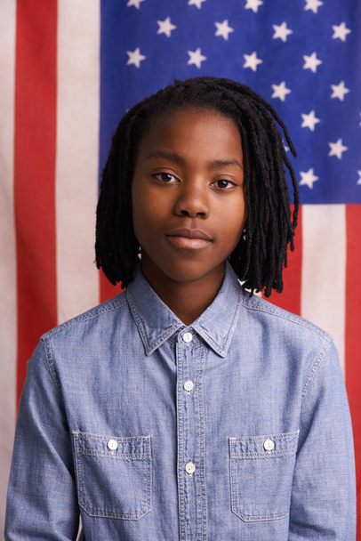 Pledging his allegiance. Portrait of a confident young boy standing in front of an American flag - 写真・画像