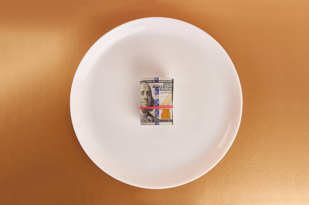 Egy fehér tányér egy tekercs dollárral arany alapon.. - Fotó, kép