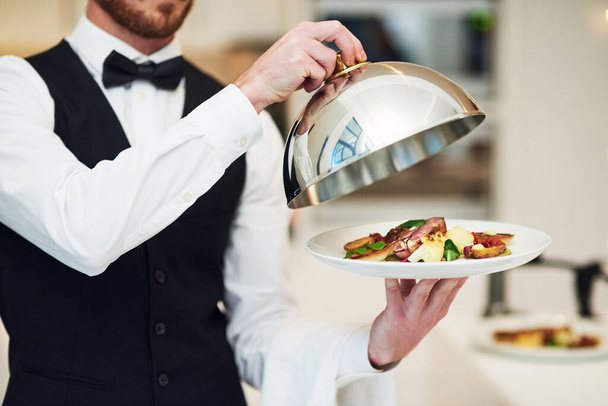 Waiter, hands and opening plate of food for serving, meal or customer service at indoor restaurant. Man employee caterer or server catering or bringing open dish for fine dining, hospitality or order. - Fotografie, Obrázek
