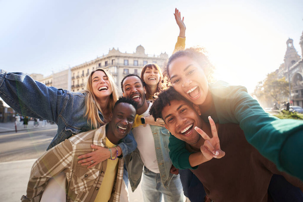 Eine Gruppe fröhlicher Studenten College-Freunde, die gemeinsam Spaß haben, während sie durch europäische Städte reisen. Glückliche Gemeinschaft unterschiedlicher Menschen. Selektiver Fokus auf das Selfie mit dem smily-Paar. - Foto, Bild