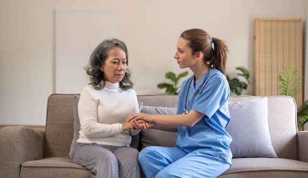 Happy patient is holding caregiver for a hand while spending time together. Elderly woman in nursing home and nurse... - Photo, Image