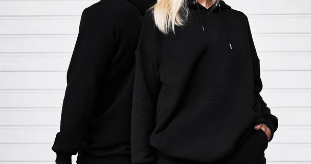 Mann und Frau tragen schwarzen Kapuzenpulli ohne Logo. Langärmelige, dunkle Sweatshirt-Attrappe. Grundlegende Bekleidung. - Foto, Bild