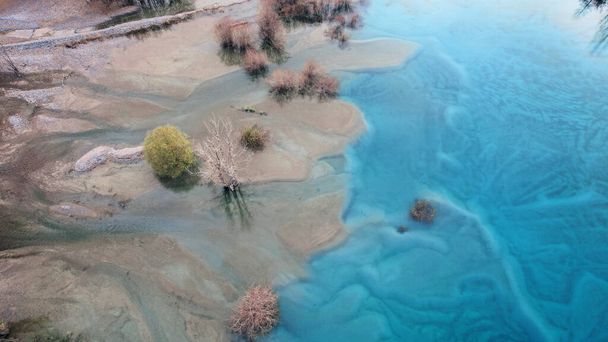 Turkuaz mavi ayna suyu ve gölde ağaçlar. Su altı akıntılarından gelen ışık çizgileri görülebilir. Sonbahar dağları ve kozalaklı ağaçlar suya yansıyor. Issyk Dağı Gölü, Kazakistan - Fotoğraf, Görsel