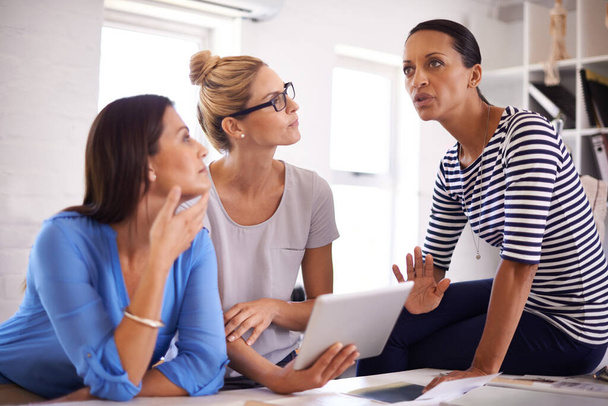 Sharing insights and ideas. Three businesswomen brainstorming ideas while gathered around a digital tablet - Foto, Bild