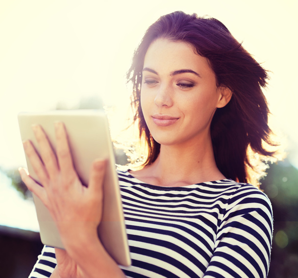 Περιηγείται τις αγαπημένες της ιστοσελίδες. μια όμορφη νεαρή γυναίκα χρησιμοποιώντας ένα ψηφιακό δισκίο, ενώ στέκεται έξω στο φως του ήλιου - Φωτογραφία, εικόνα