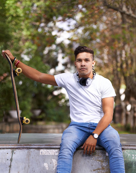 Skateboarden - een kunstvorm, een levensstijl en een sport. een jonge man neemt een pauze tijdens het skateboarden - Foto, afbeelding