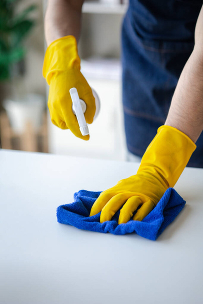 Odayı temizleyen kişi, temizlik personeli şirket odasındaki camları silmek için bez ve dezenfektan kullanıyor. Temizlik personeli. Organizasyondaki temizliği sürdürmek. - Fotoğraf, Görsel