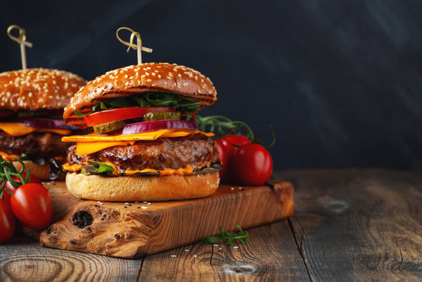 Twee heerlijke zelfgemaakte hamburgers van rundvlees, kaas en groenten op een oude houten tafel. Dikke ongezonde voeding close-up. met kopieerruimte. - Foto, afbeelding