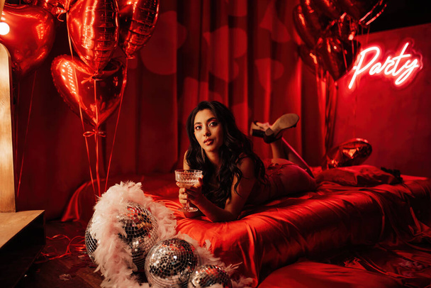 Kiharat mustat hiukset aasialainen malli samppanjaa lasi poseeraa sängyssä Ystävänpäivä - Valokuva, kuva