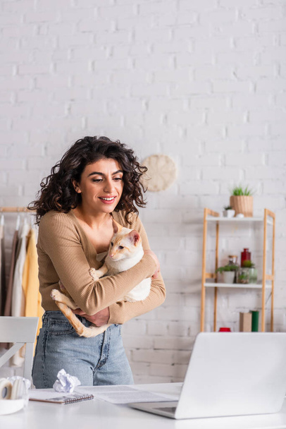 Positive freelancer holding oriental cat near laptop at home  - Photo, Image