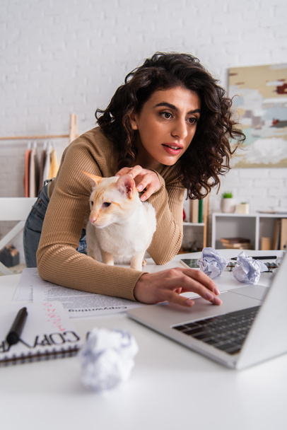 Copywriter usando laptop perto de gato oriental e papéis em casa  - Foto, Imagem