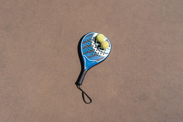 Vista dall'alto delle palle di padel gialle posizionate sulla racchetta blu sul campo marrone nella giornata di sole - Foto, immagini