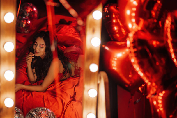 Reflexe v zrcadle asijského modelu v krajkovém prádle ležícím na posteli s červeným hedvábným prostěradlem - Fotografie, Obrázek