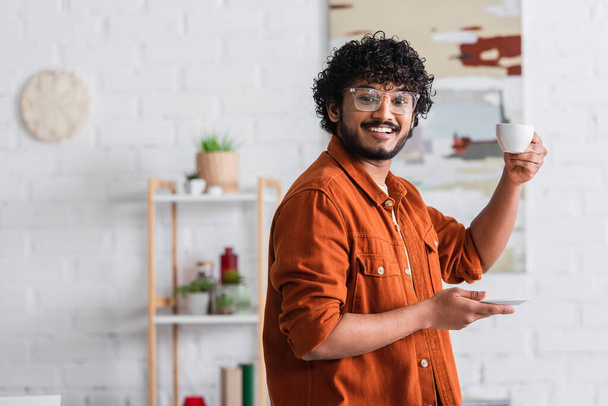Sorrindo homem indiano em óculos segurando xícara de café em casa  - Foto, Imagem