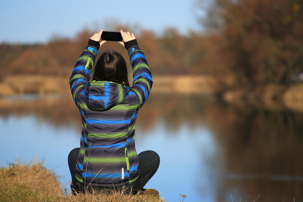 Νεαρό κορίτσι χρήση της κινητής τηλεφωνίας για τη λήψη φωτογραφιών - Φωτογραφία, εικόνα