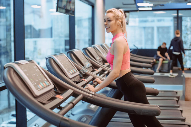 Side view of two attractive sports women on running track. Attractive young sports woman is working out in gym. Running on treadmill. - Photo, Image