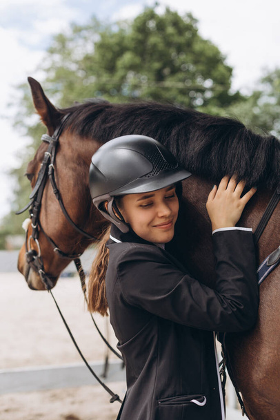 Vrouw in de buurt van paard. Ruiter in een zwart uniform, met helm op - Foto, afbeelding